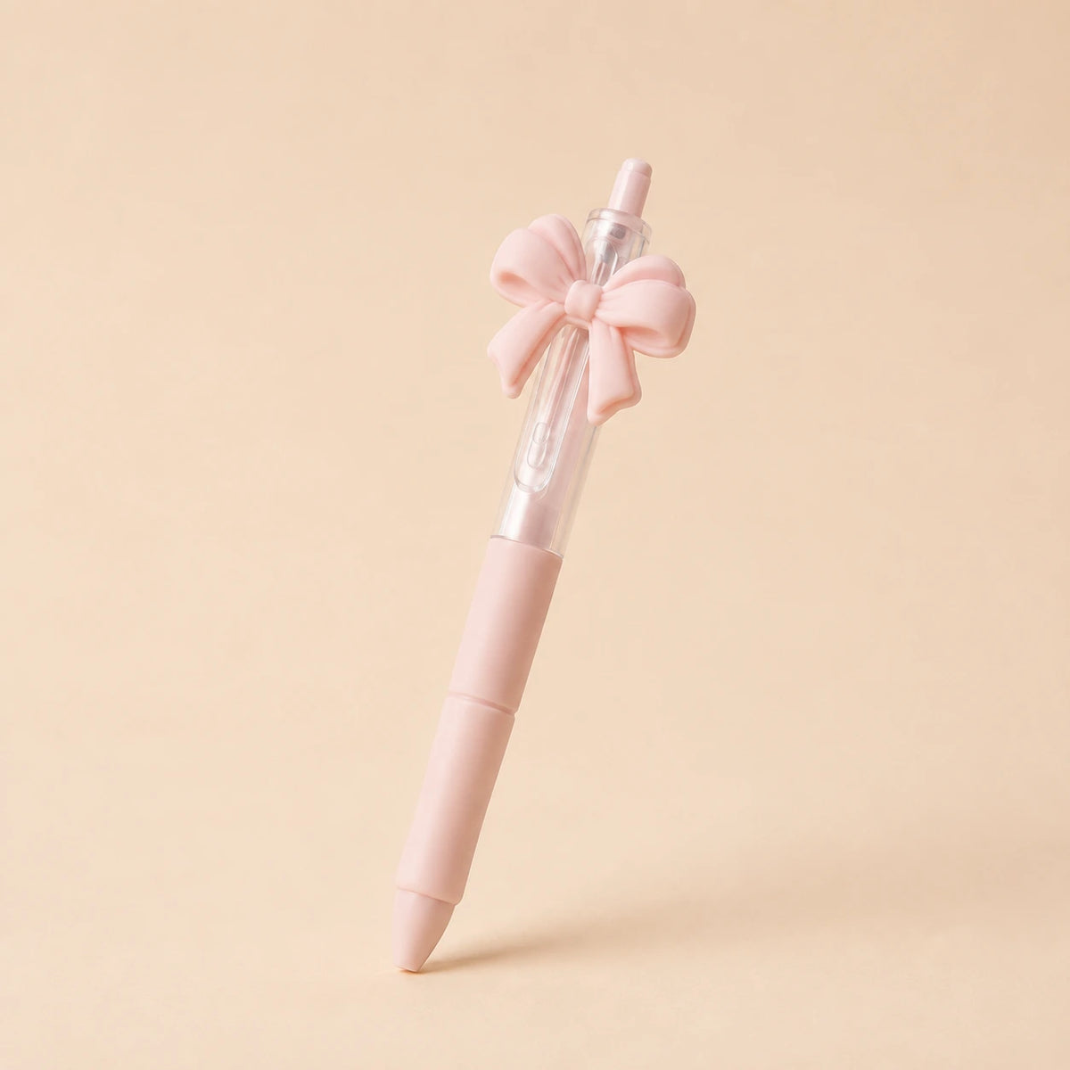 A pastel pink retractable pen with a decorative pink bow on the cap, standing upright on a solid beige background.